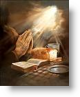 Hands praying with bread and Bible on a table illuminated by sunlight.
